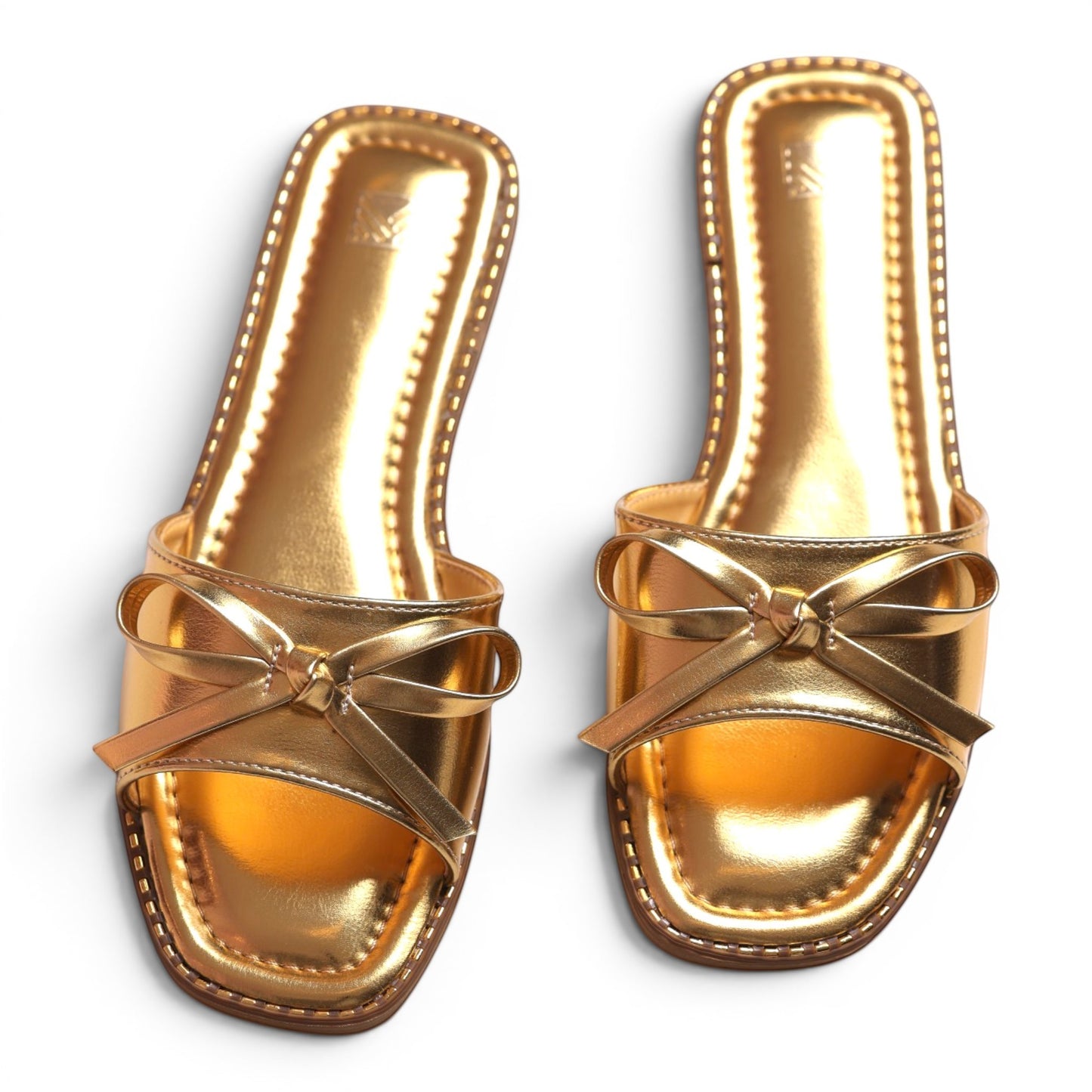 Moda Ugo patent gold slide sandals with square toe and bow detail. Shiny metallic finish.