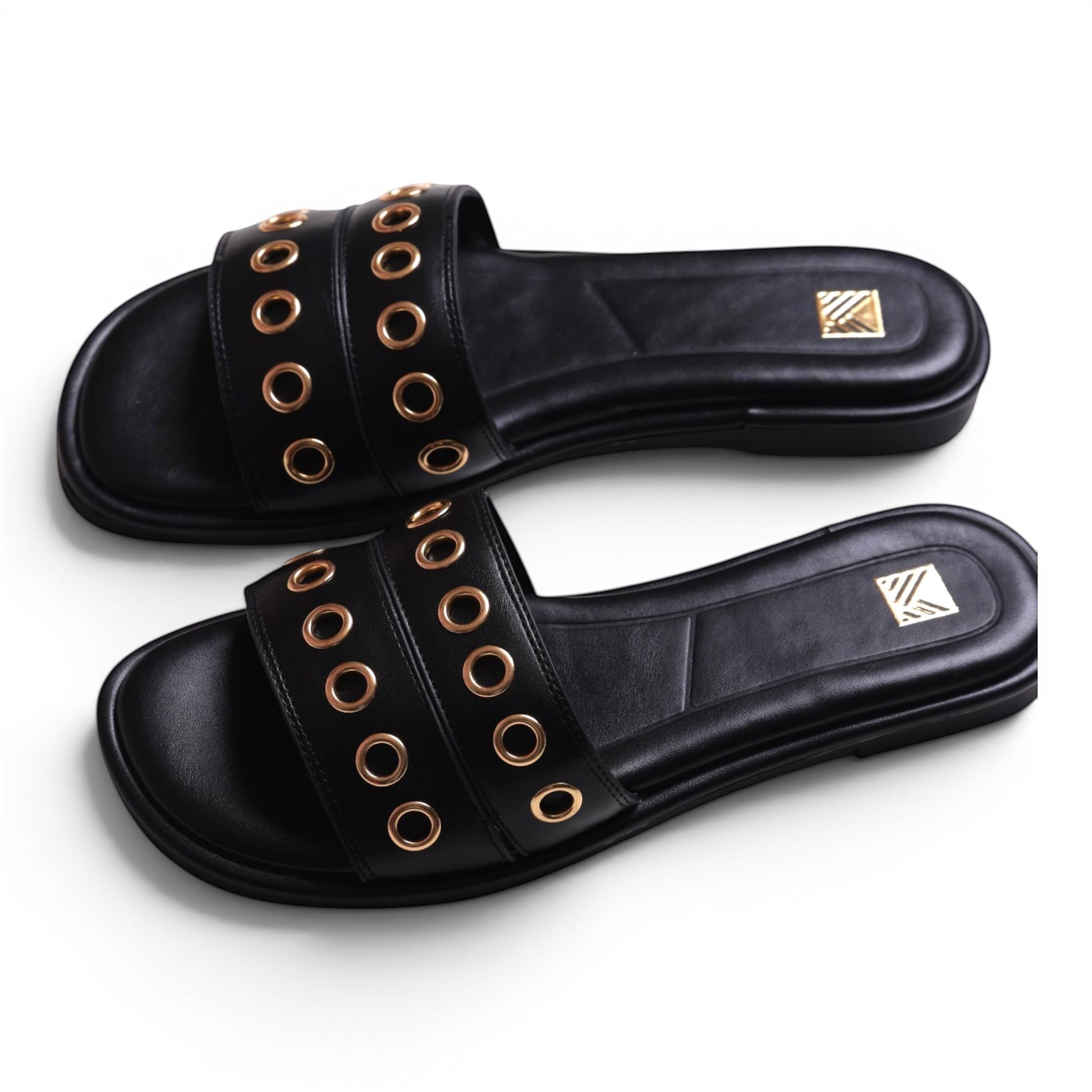 Moda Ug black leather slide sandals with gold eyelet details and a flat sole.