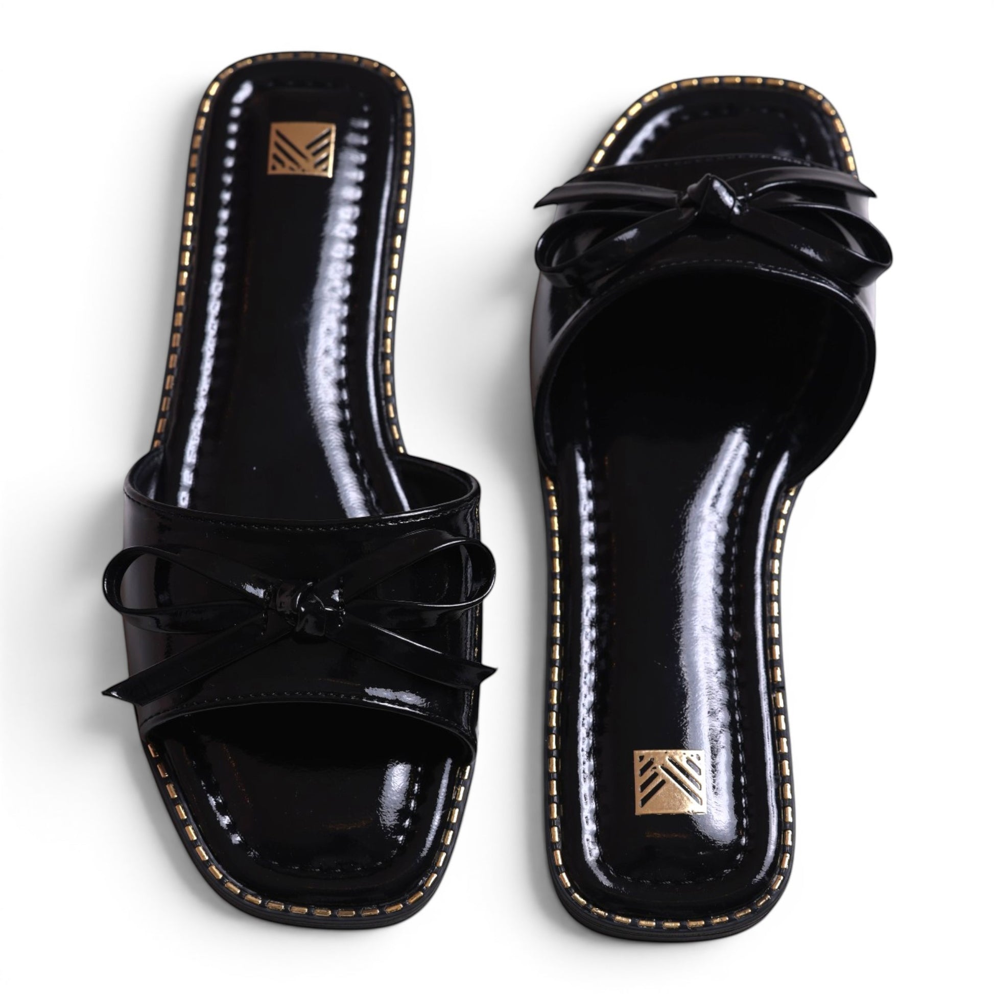 Moda Ug black patent leather slide sandals with bow detail and gold trim. Square toe.