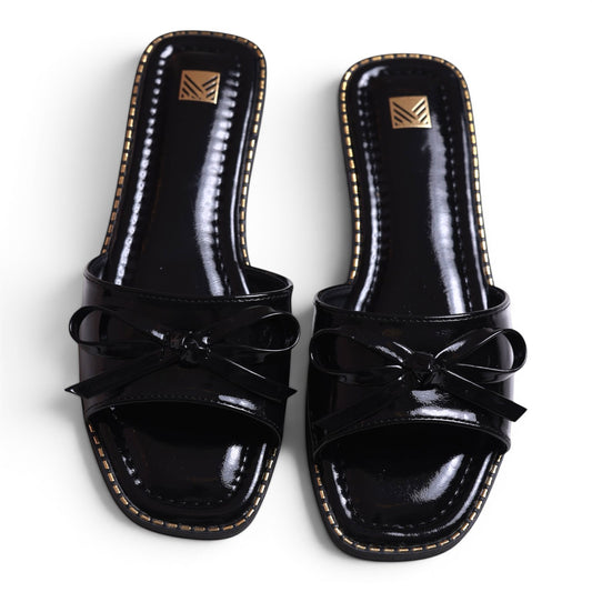 Moda Ug black patent leather slide sandals with bow detail and gold trim. Square toe.