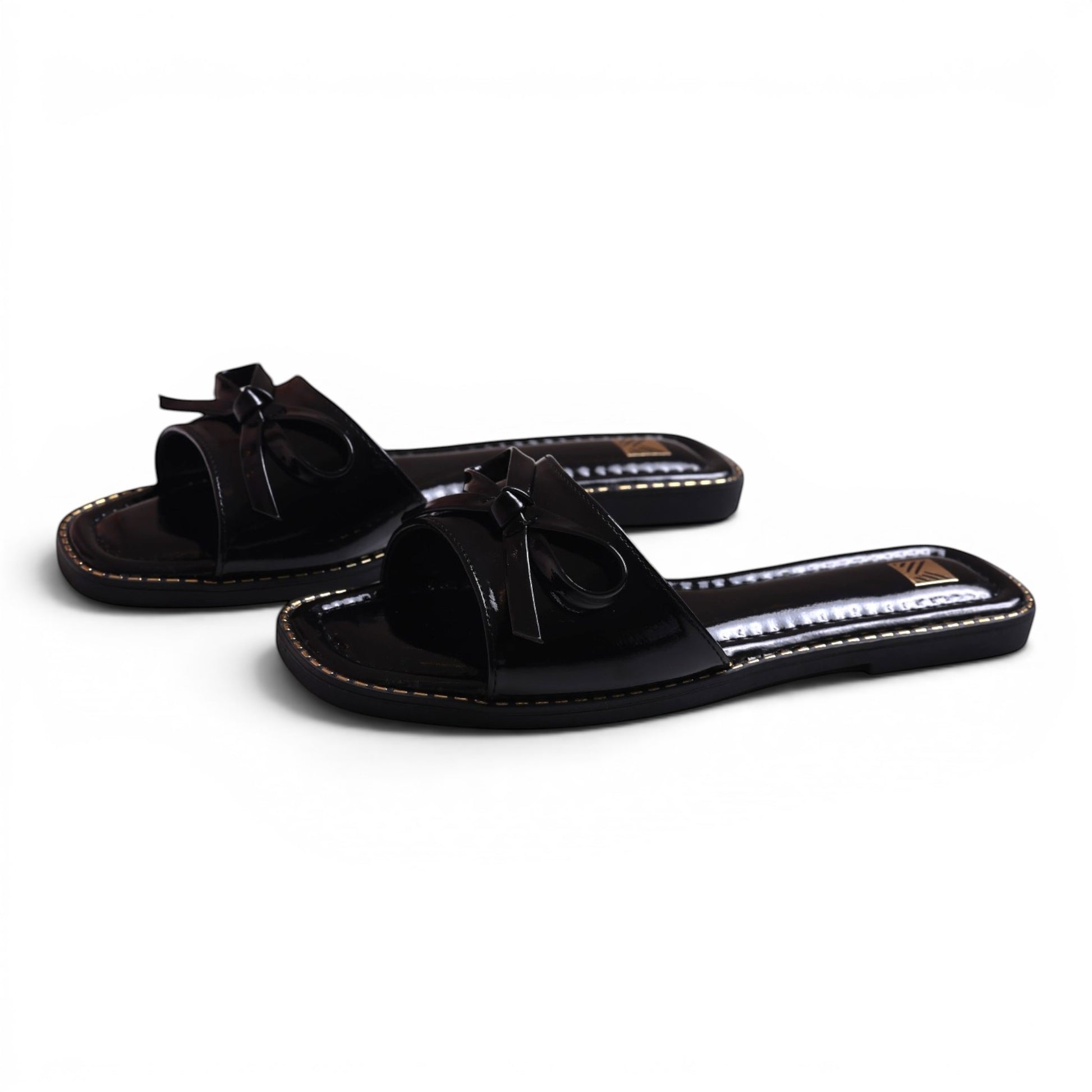 Moda Ug black patent leather slide sandals with bow detail and gold stitching. Square toe.