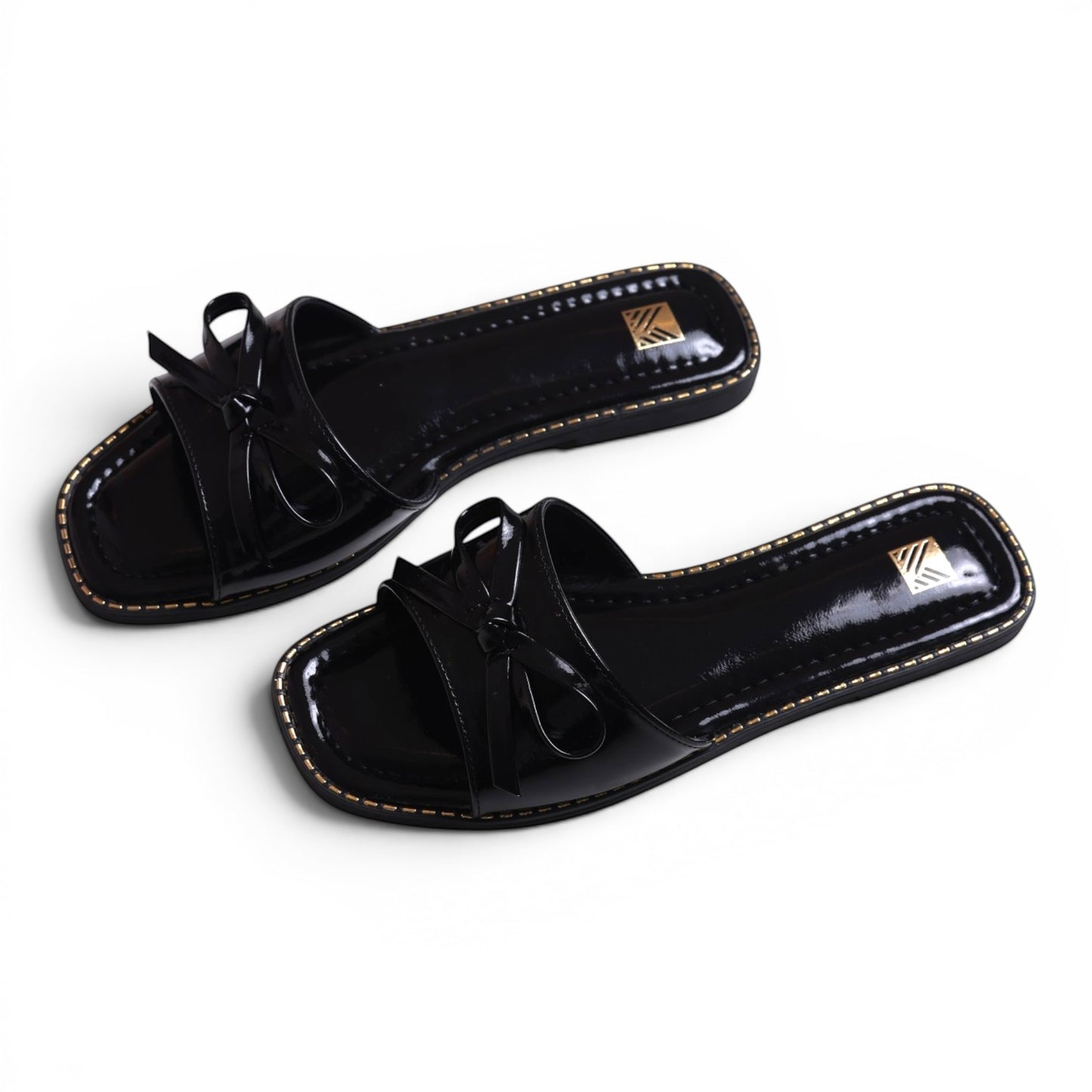Moda Ug black patent leather slide sandals with bow detail and gold trim. Square toe.