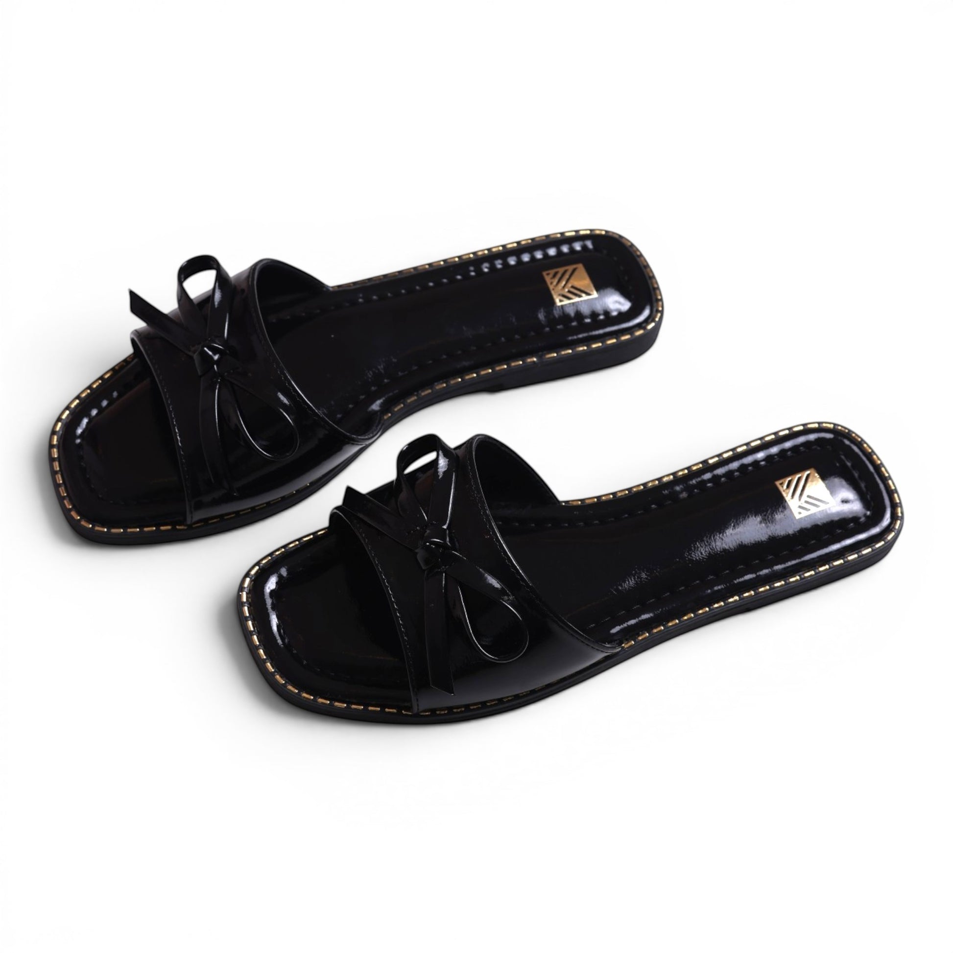 Moda Ug black patent leather slide sandals with bow detail and gold trim. Square toe.