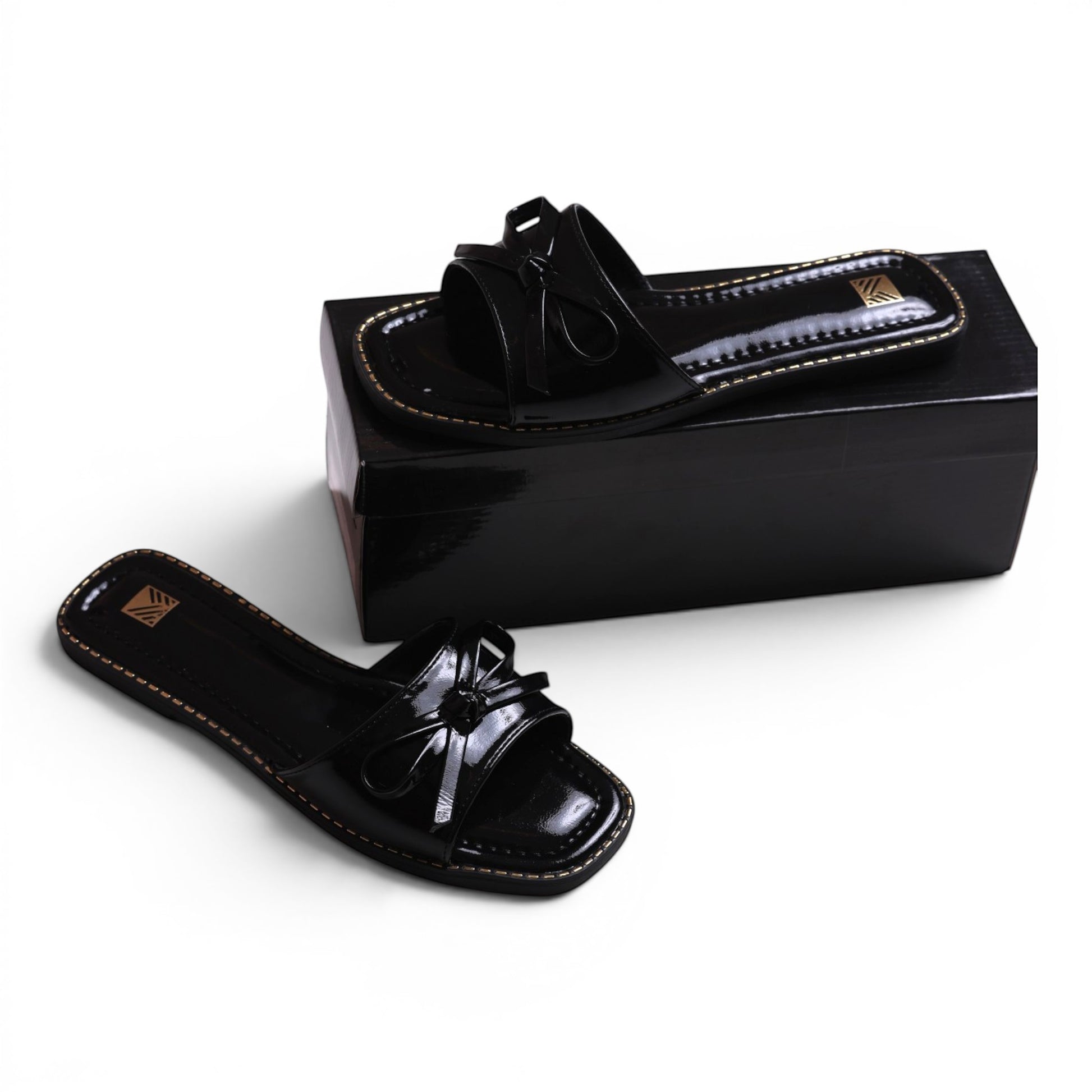 Moda Ug black patent leather slide sandals with bow detail and gold stitching. Square toe.