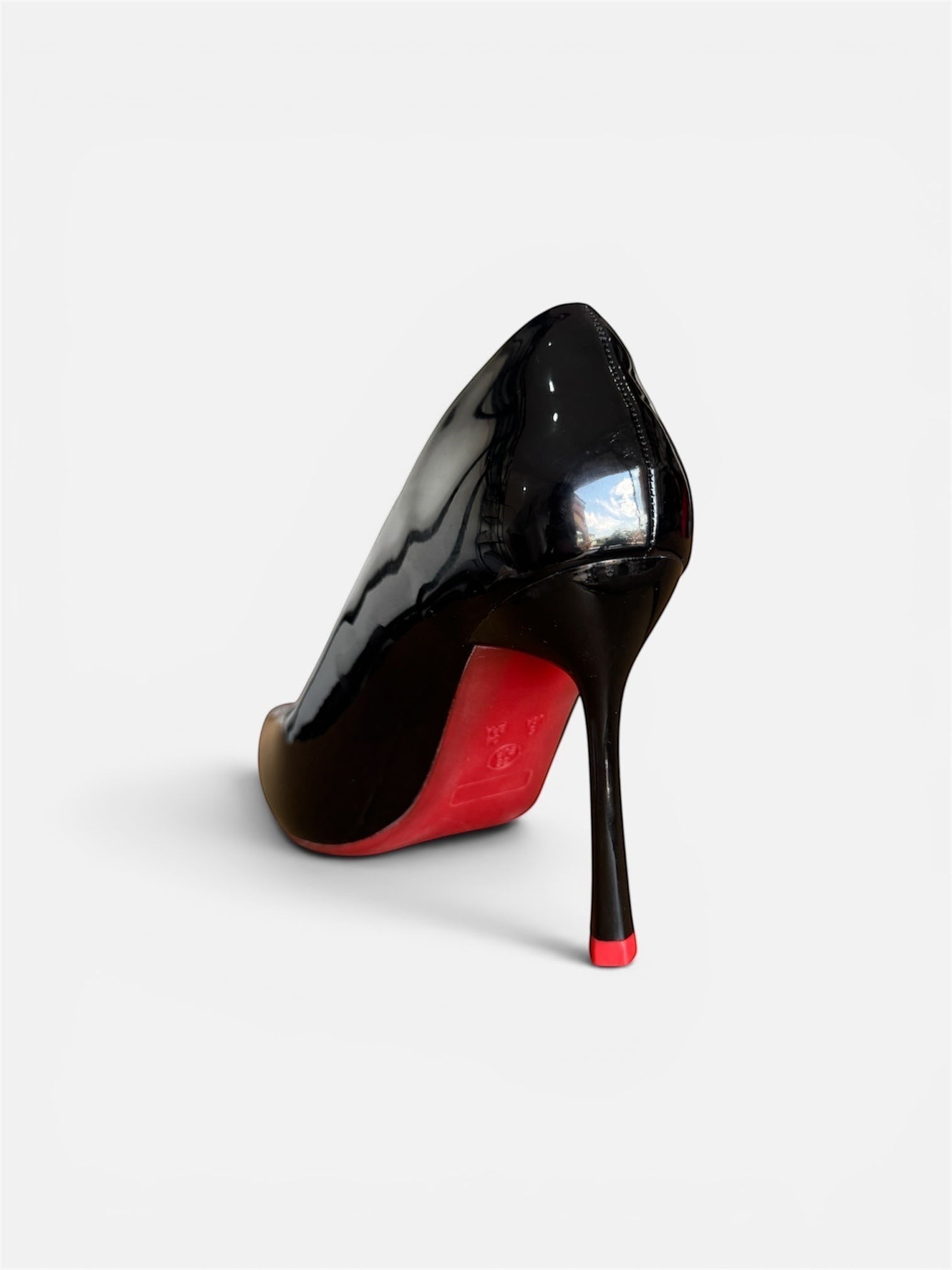 Moda Ug black patent leather pointed toe high heel pumps with a red sole and a small red accent on the heel tip.