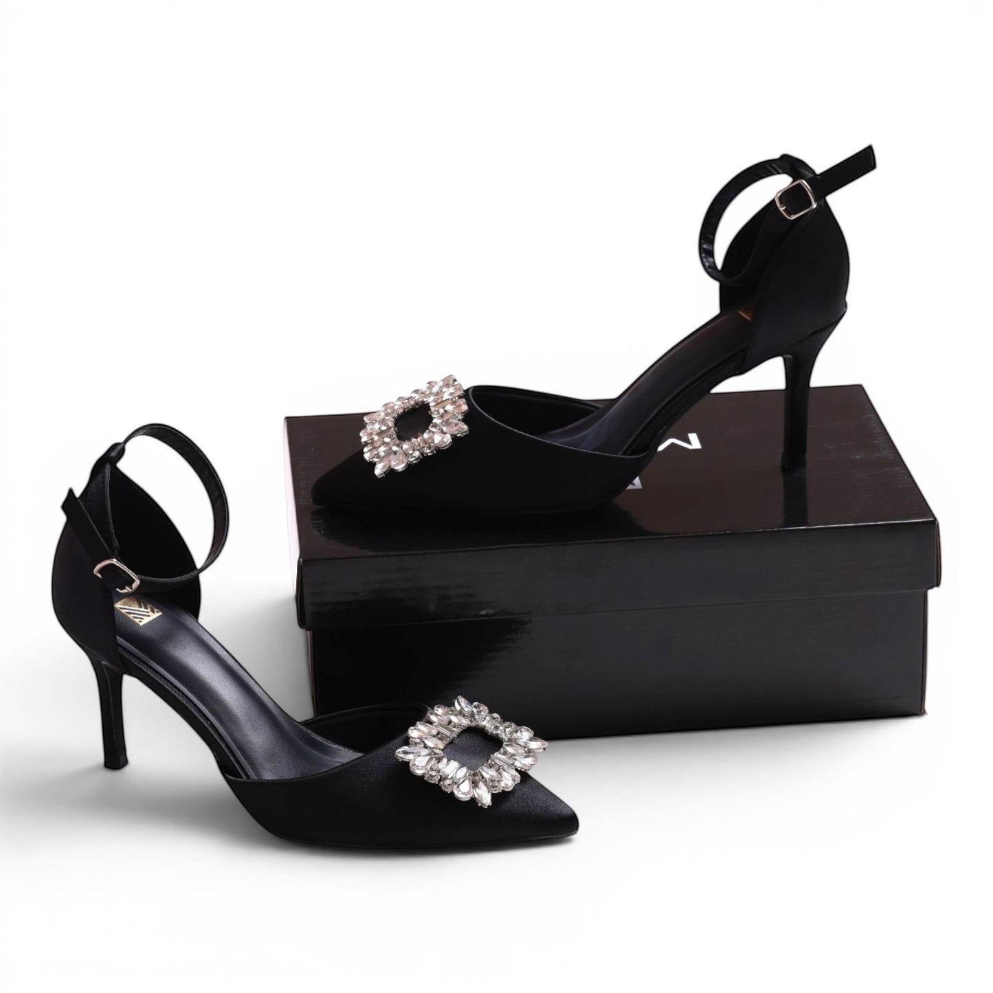 Moda Ug black satin pointed-toe heels with ankle strap and crystal buckle detail.