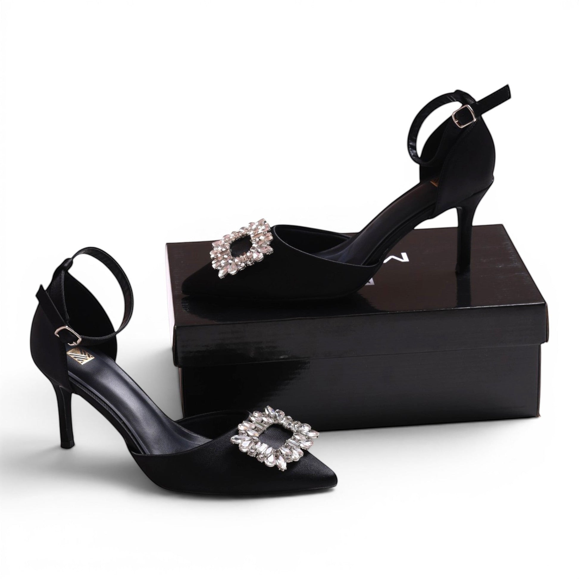 Moda Ug black satin pointed-toe heels with ankle strap and crystal buckle detail.
