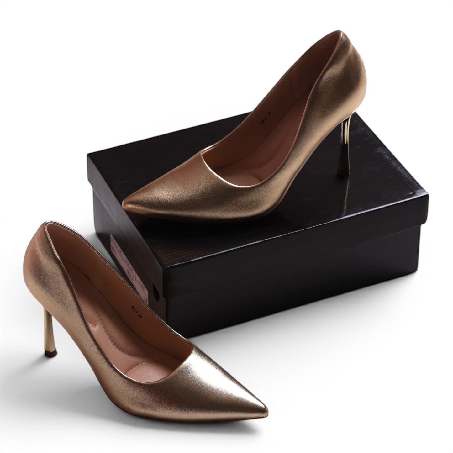 Moda Ug gold metallic pointed-toe stiletto heels with a sleek design, presented on a black shoebox.