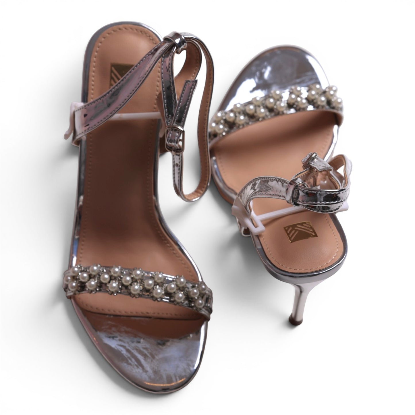 Moda Ug silver metallic stiletto sandals with pearl-embellished strap and ankle buckle closure.